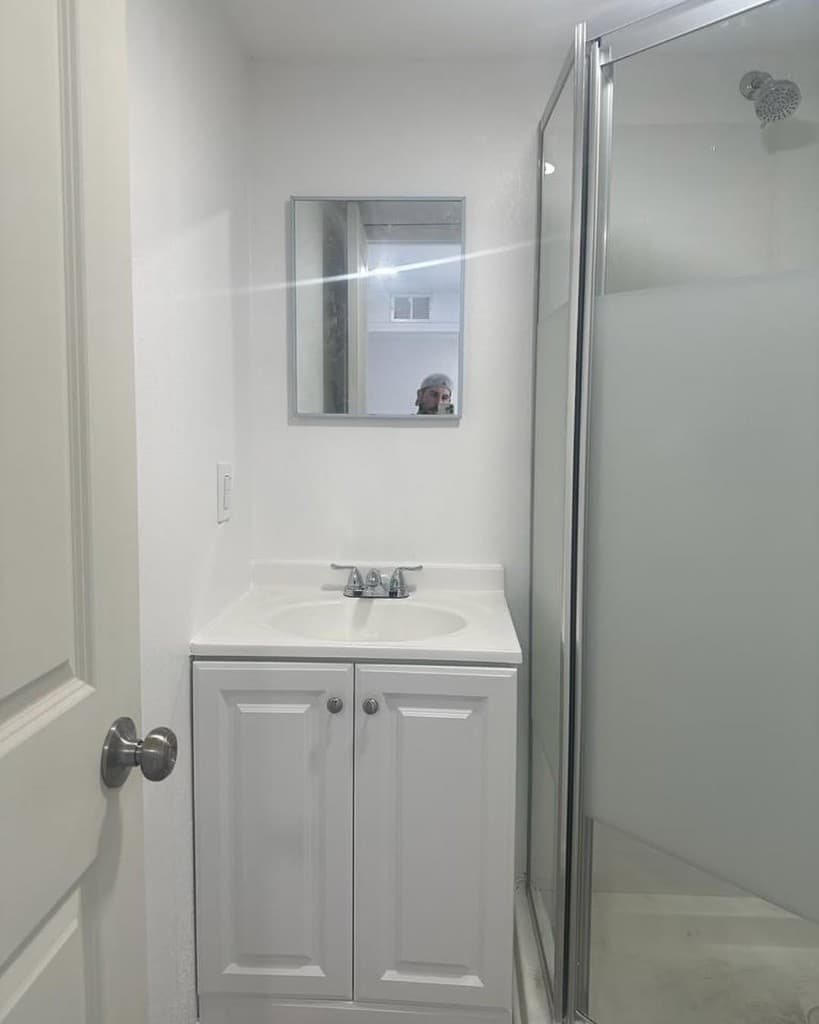 Bright small bathroom white vanity oval sink mirrored cabinet and framed glass shower to the side.
