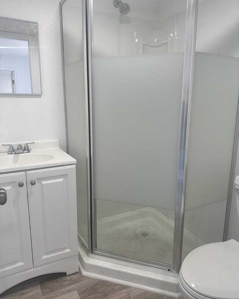 Bathroom neo angle shower brushed chrome framed glass white vanity chrome faucet wood look tile floor daylight.