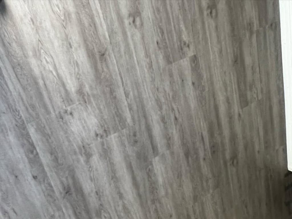 Close luxury vinyl planks cool grey knots grain staggered doorway white casing bottom right corner cropped.