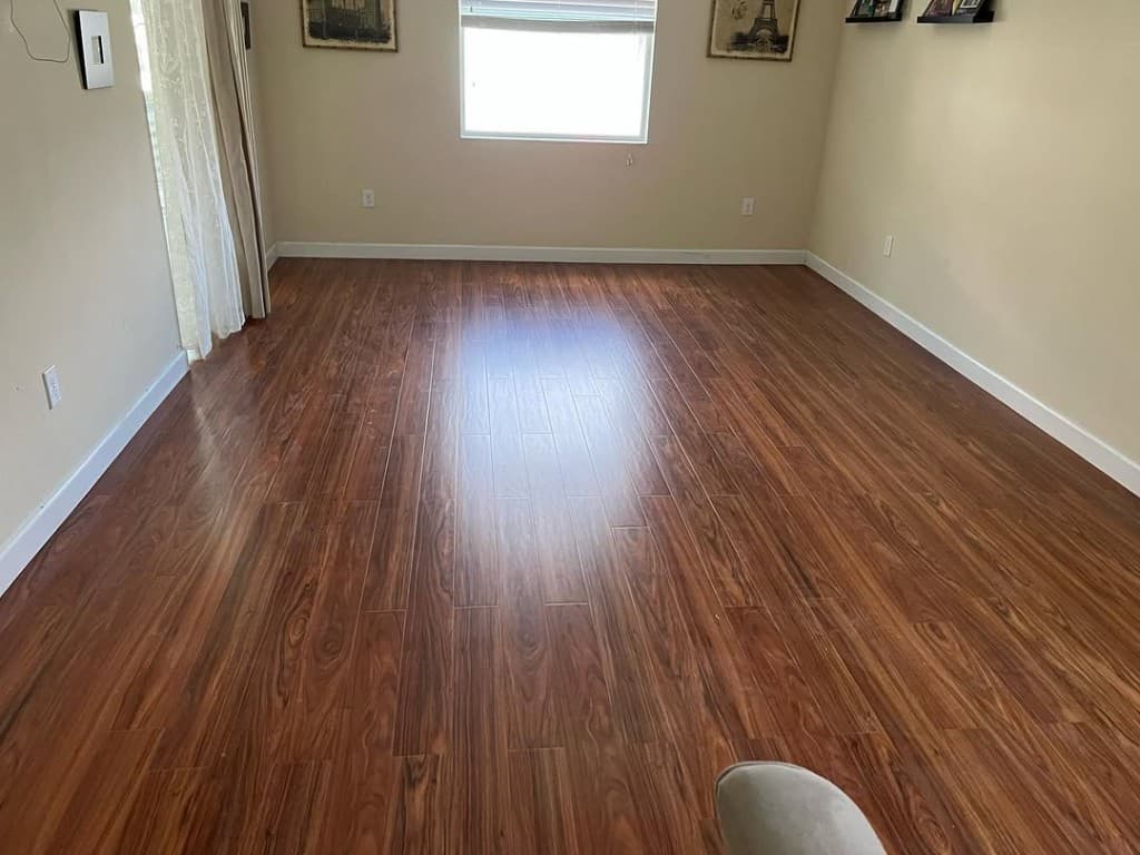 Empty room reddish wood laminate planks glossy reflections beige walls sliders window frames symmetrical decor prints.