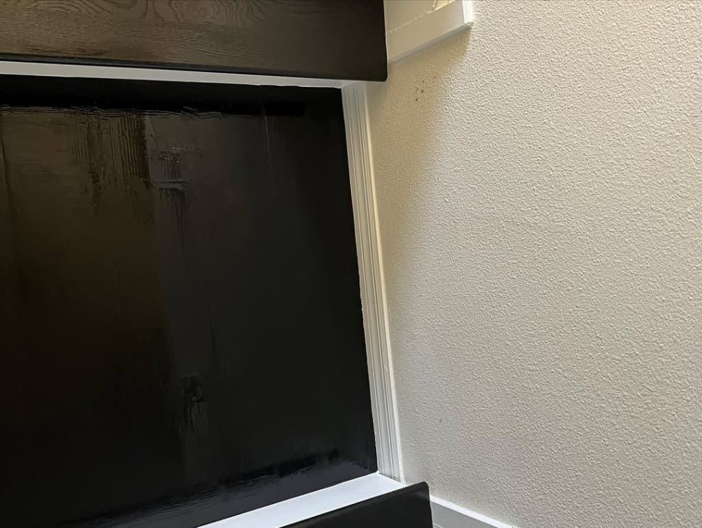 Macro intersection glossy black cabinetry white shoe mould textured beige wall precise paint brush direction visible.