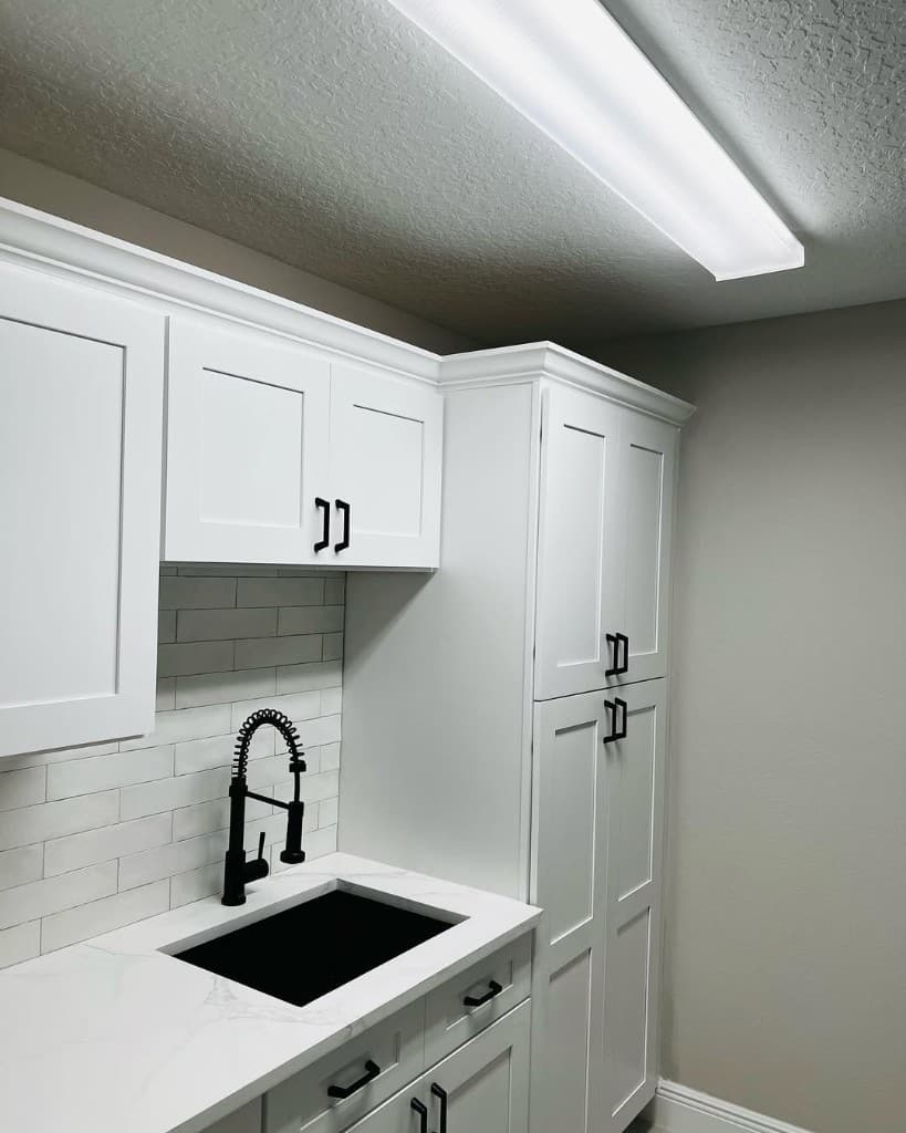 Bright kitchen or utility room with white shaker cabinets, LED ceiling panel, marble-look counter, and tall pantry.