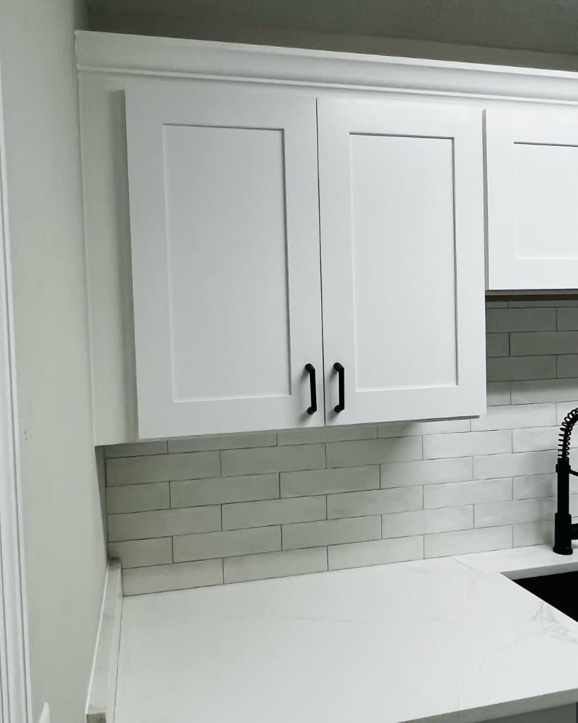 Close-up of white shaker kitchen cabinets, subway tile backsplash, and veined white countertop with a black faucet.