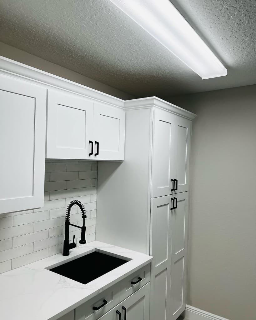 Black undermount sink with a high-arc black faucet, white veined countertop, and shaker cabinets with black pulls.
