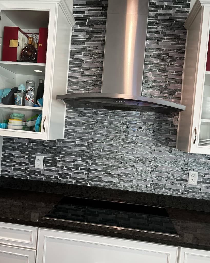 Kitchen chimney stainless hood metallic mosaic backsplash black glass cooktop white shaker glass door cabinet symmetrical outlets photography.