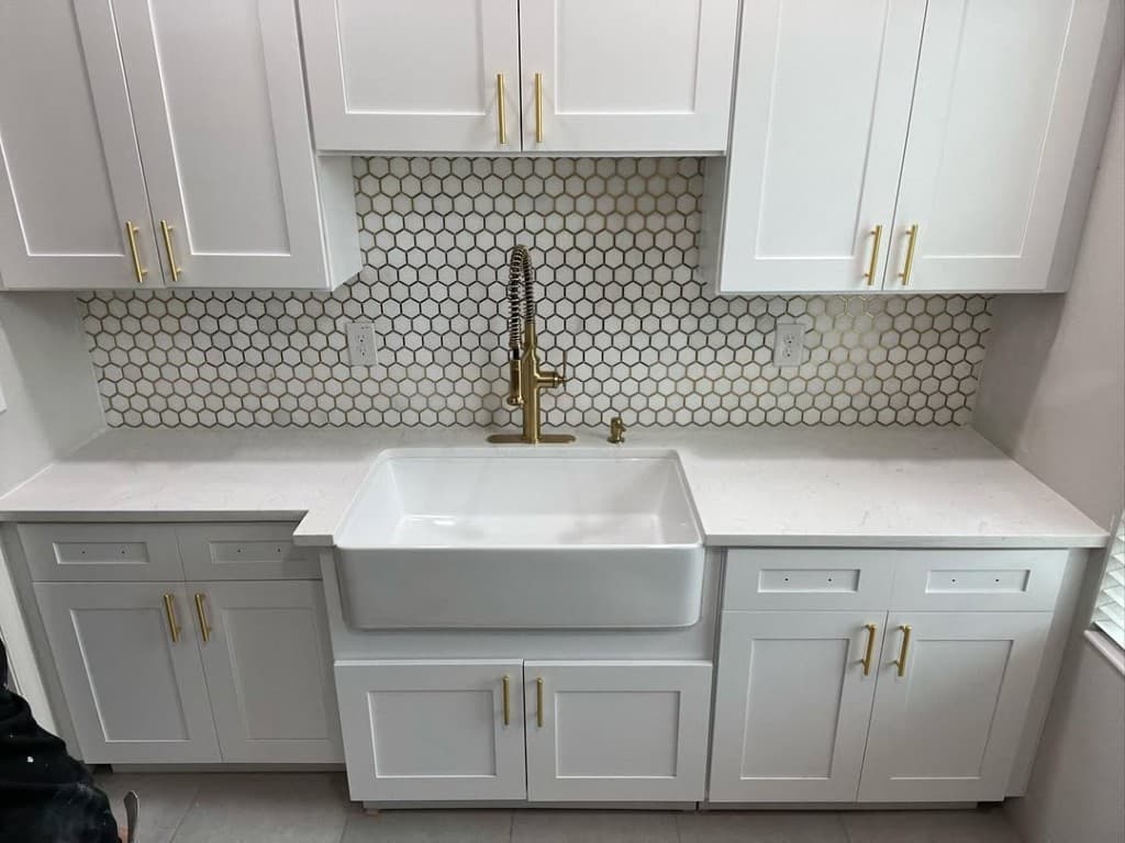 Wide symmetrical kitchen wall gold spring faucet apron sink white shaker gold hardware double outlet honeycomb backsplash.