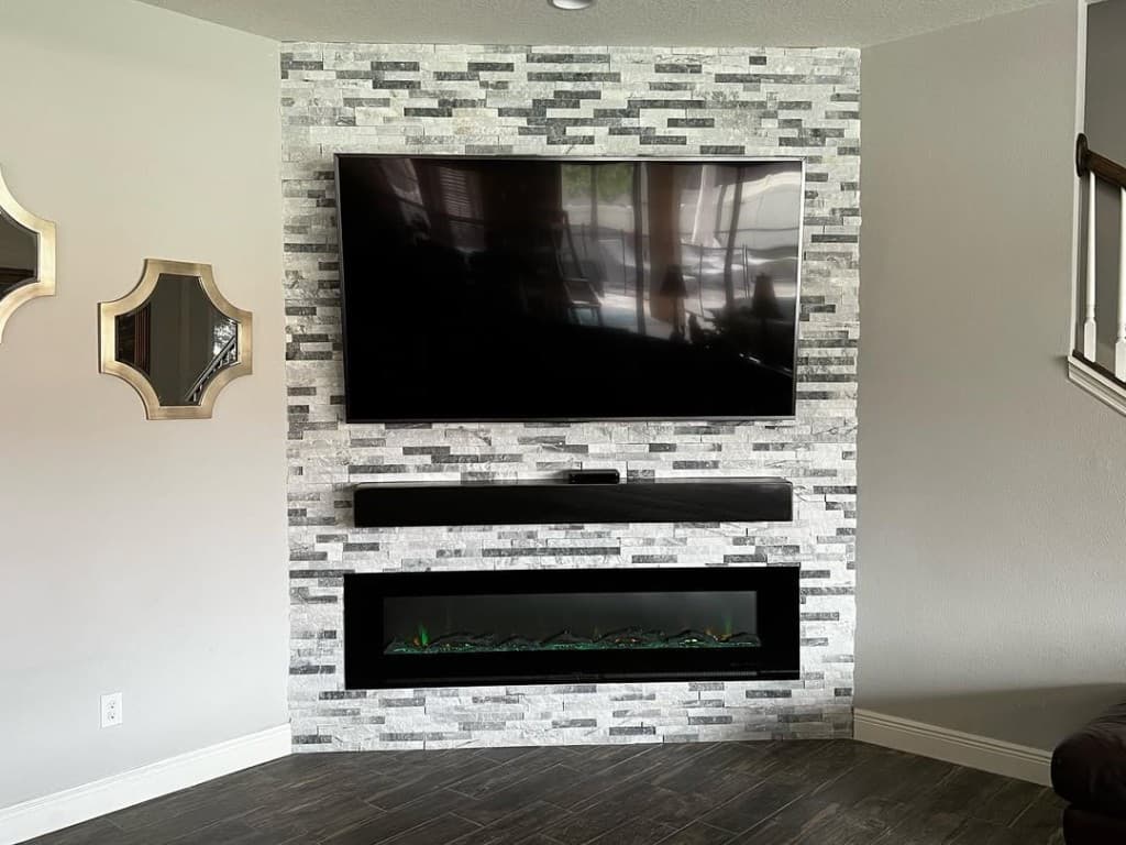 Living stacked stone accent large TV electric fireplace glossy dark floor tile symmetrical grey walls flank.